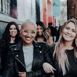 A group of friend are walking down a city street, smiling.