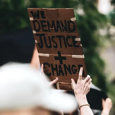 Protest sign held up in the air reading "we demand justice and change"