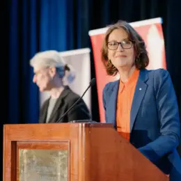 Emcee Gloria Macarenko from CBC stands behind a podium.