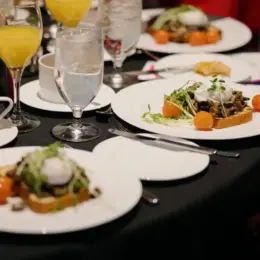Mushroom toast is displayed on white dishes on a table with a black tablecloth.