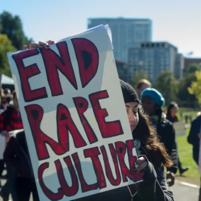 Young woman carrying protest sign that reads "End rape culture".
