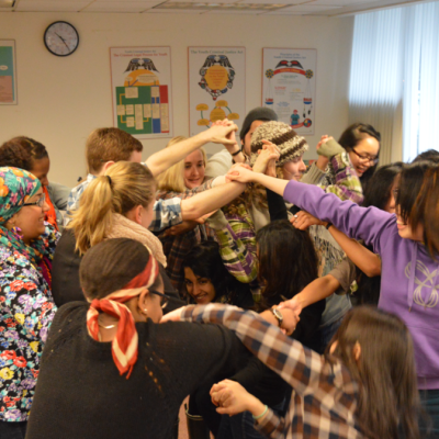 A group of people holding hands try to untangle themselves at a workshop.