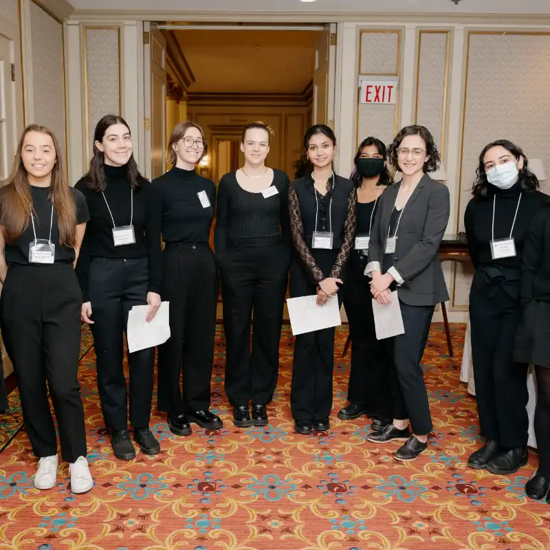 A group of volunteers dressed in black and wearing nametags stand in a semi-circle at the Equality Breakfast.