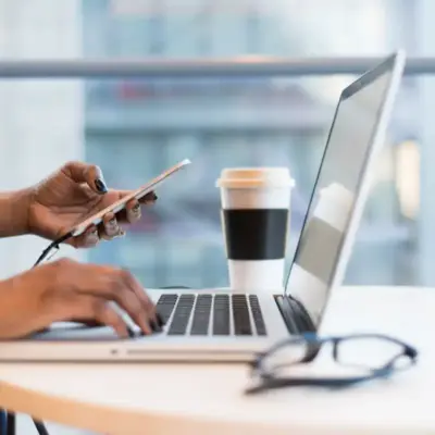 Someone is typing on a laptop and holding a cellphone.