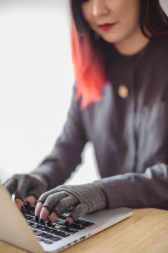 Woman typing on computer wearing fingerless gloves. 