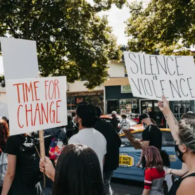 People hold signs saying "time for change" and "silence is violence" while walking in a peaceful protest. 