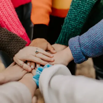 A group of people are standing in a circle with their hands brought together in the middle. 