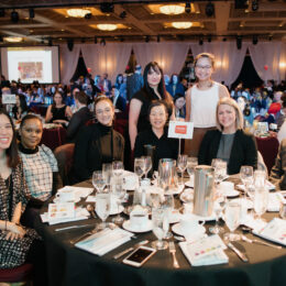 A group of Breakfast attendees are circled around their table smiling.