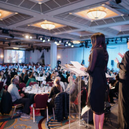 Emcee Anita Bathe welcomes attendees into the ballroom from the stage.