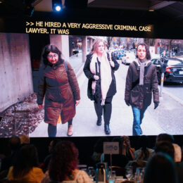 A still image of a short documentary made about the Single Mothers' Alliance test case is playing on a large screen above the stage.