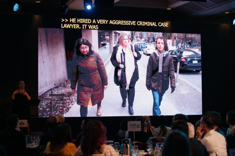 A still image of a short documentary made about the Single Mothers' Alliance test case is playing on a large screen above the stage.