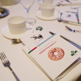 A table setting on a white table cloth with an event program in the middle.