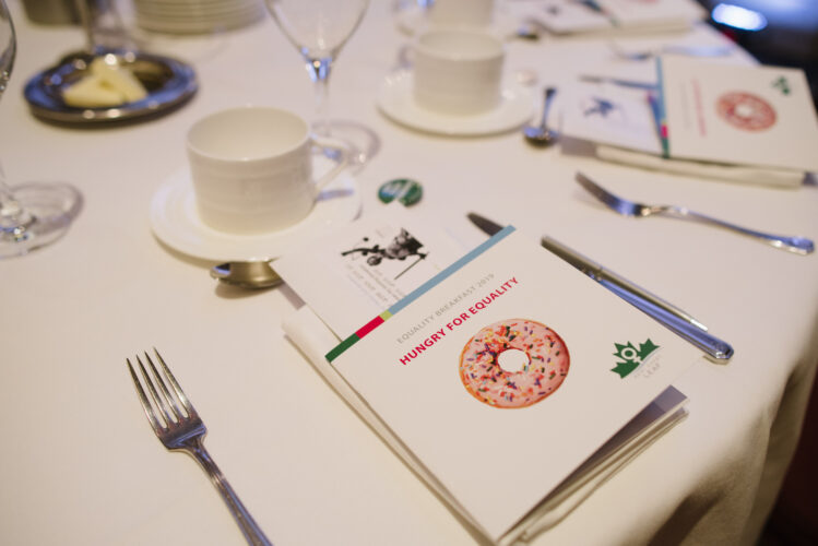 A table setting on a white table cloth with an event program in the middle.