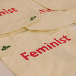 Canvas tote bags on a table that say "Feminist" in pink letters.