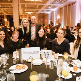 A group of Equality Breakfast attendees smile while sitting around a large table.