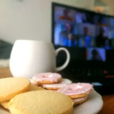 A plate of cookies and mug of tea sit on a table in front of a Zoom meeting with several participants.