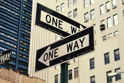 Intersecting signs denoting a One Way Street with high rise buildings behind them.