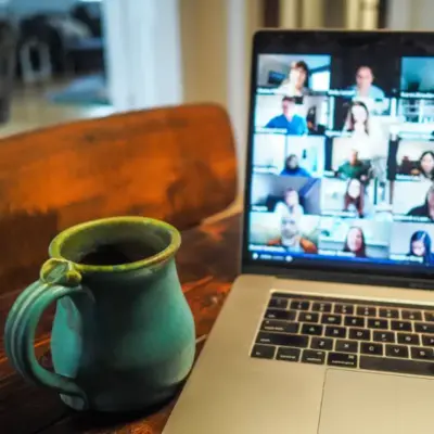 A blue ceramic mug sits on a table in front of a laptop. The screen shows several people participating in an online meeting.