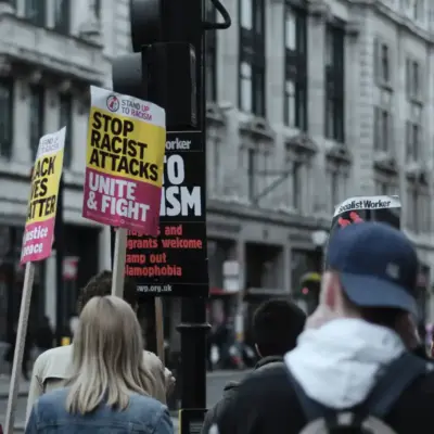 A group of people march in a street holding signs that say "Stop racist attacks. Unite and fight"