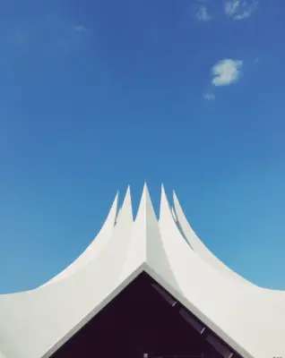 Image of a white tent with multiple points at the top with a bright blue sky and one cloud in the background