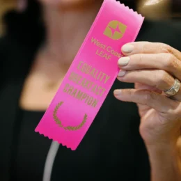 A close up of a pink ribbon given to donors that says "West Coast LEAF Equality Breakfast Champion".