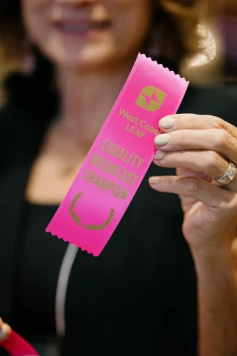 A close up of a pink ribbon given to donors that says "West Coast LEAF Equality Breakfast Champion".