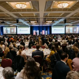 A wide shot of the full ballroom at the 2024 Equality Breakfast. Pam Palmater is delivering her keynote address from the stage, flanked by four large screens.