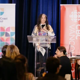 A close up of keynote speaker Pam Palmater finishing her keynote. The crowd is standing and clapping, and Pam is smiling with her hand on her heart.