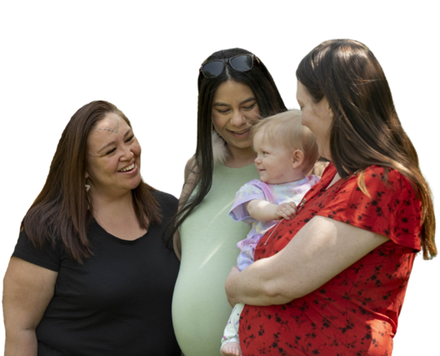 2 indigenous and one white woman surrounding a baby and smiling at them.