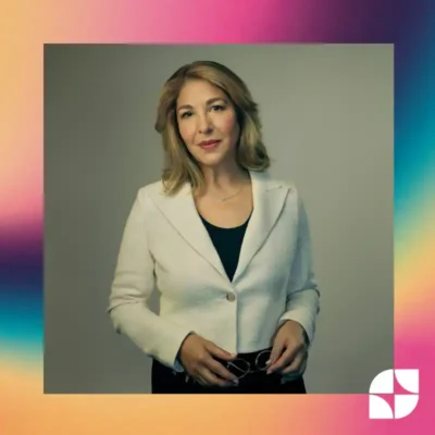 Naomi Klein in a cream blazer and black shirt holding her glasses and smiling softly. Grey background in a pixelated rainbow frame with a white West Coast LEAF logo in the bottom right corner.