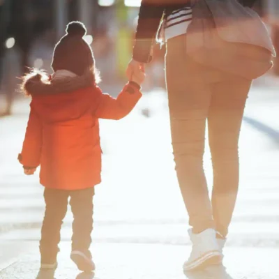 A child wearing a red winter coat is holding their parent's hand while they walk away.